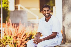 männliche Pflegefachkraft mit Migrationshintergrund lächelt in Kamera