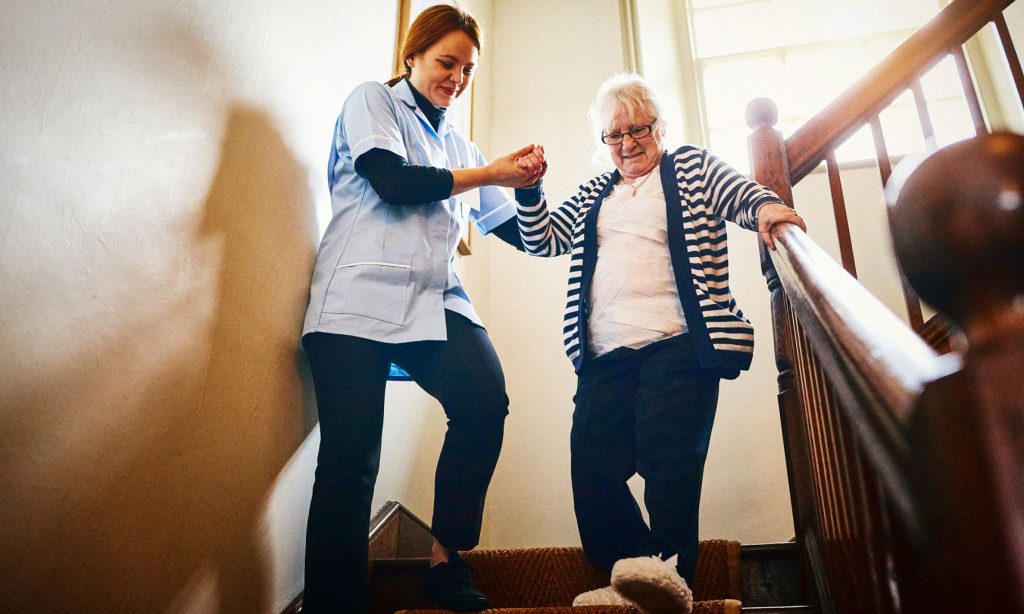 Pflegekraft unterstützt Frau beim Treppensteigen in der ambulanten Pflege