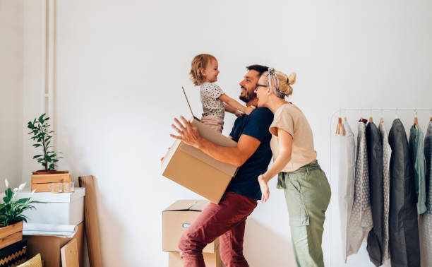 Glückliche Familie mit einem Kind beim Tragen und Auspacken von Kartons während des Umzugs in die neue Wohnung