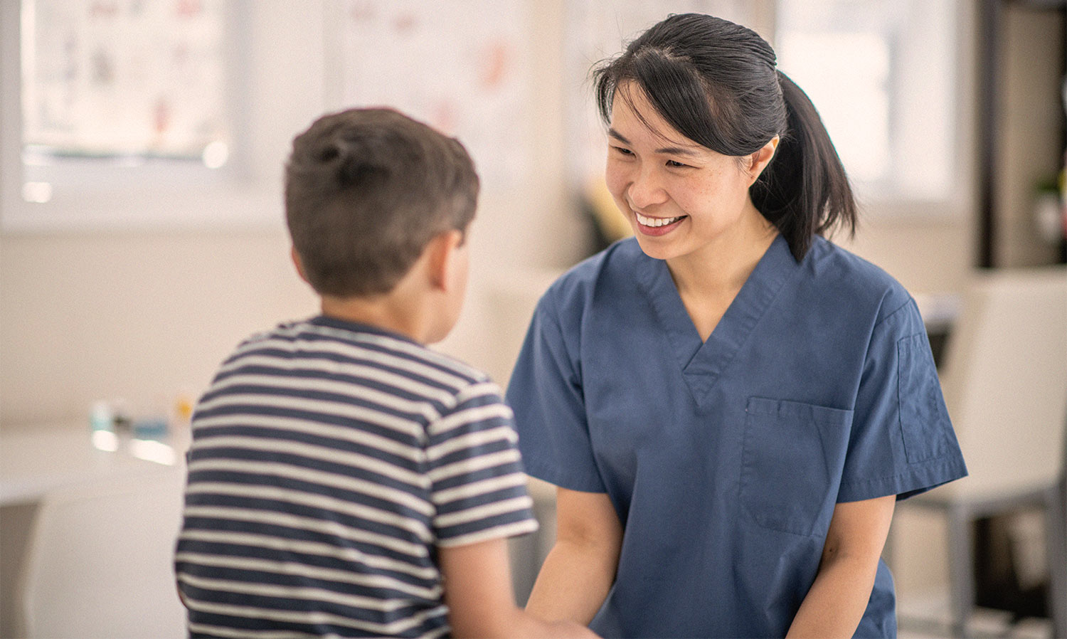 Asiatische Kinderkrankenschwester lächelt kleinen Jungen an